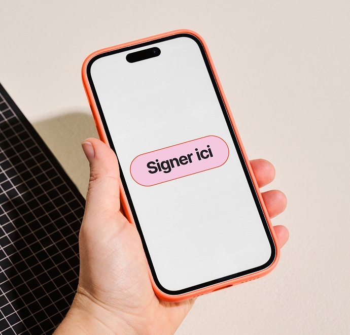 Une main tient un smartphone avec un étui de couleur corail. L'écran affiche un gros bouton rose intitulé "Signer ici" en français, suggérant une action de signature numérique. Une grille noire est visible à gauche.